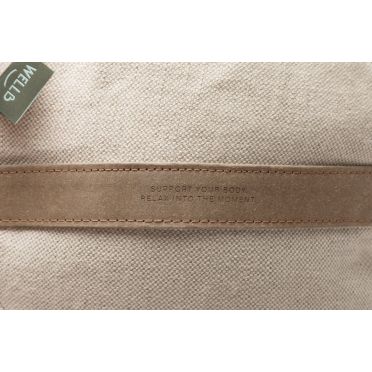 Zbliżenie na beżową poduszkę do medytacji z detalem skórzanego uchwytu z tłoczonym napisem i metką WellB, tło jednolite.